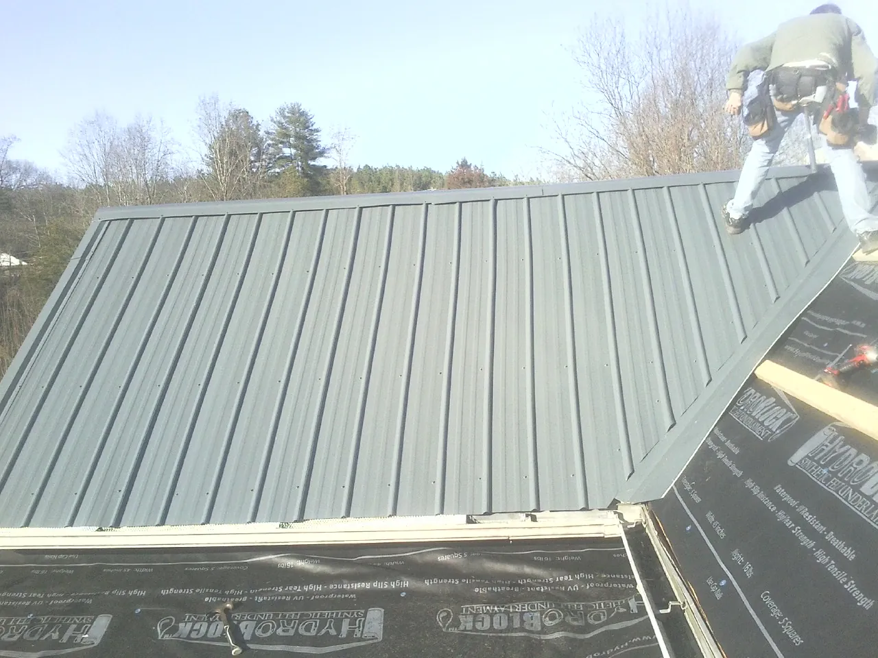 Crew installing dark green standing seam panels over synthetic underlayment in Lookout Mountain