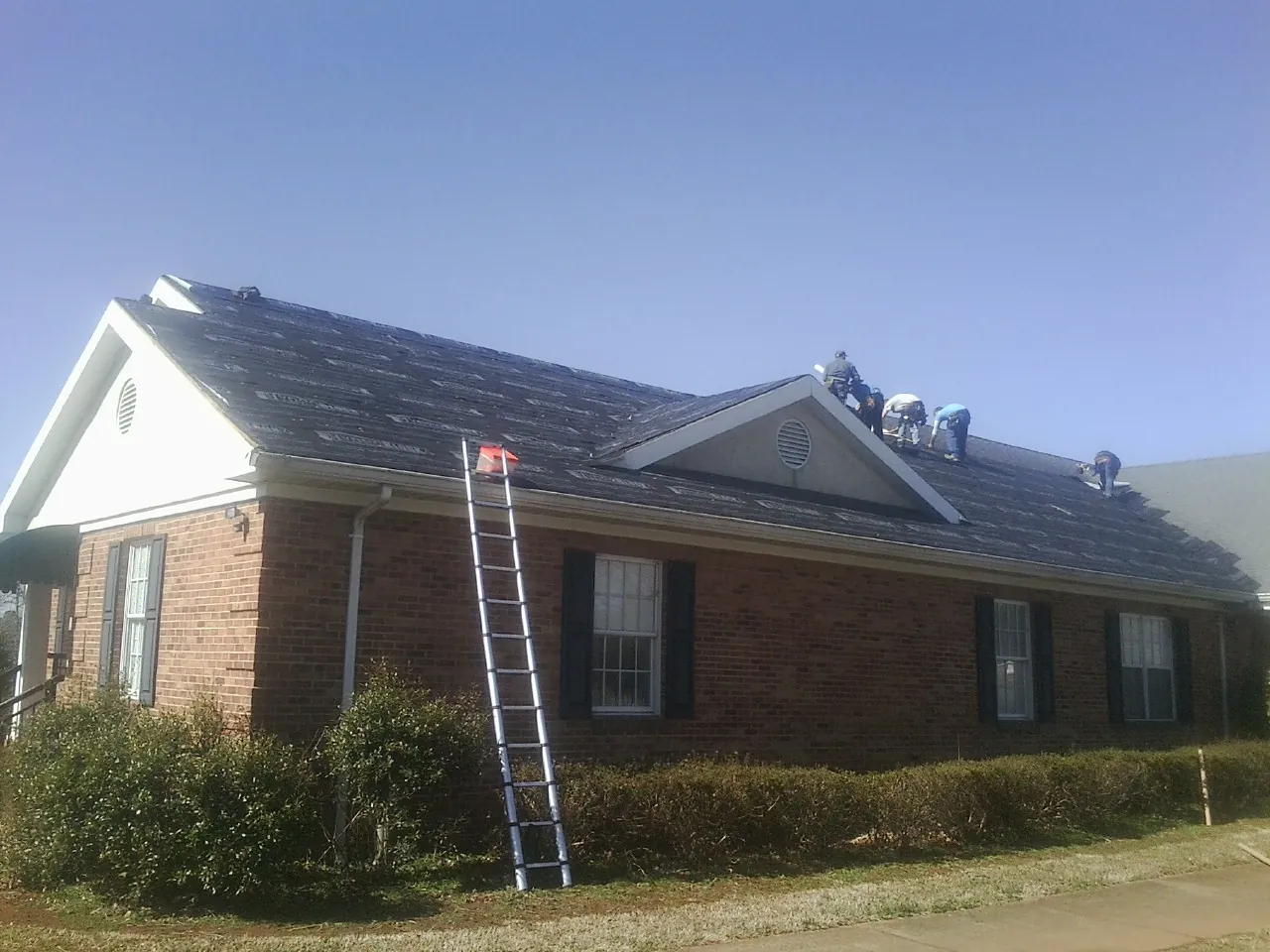 Crew tearing shingles off a brick ranch roof with a ladder set — Metal Roof Repair work by our crew in Lookout Mountain