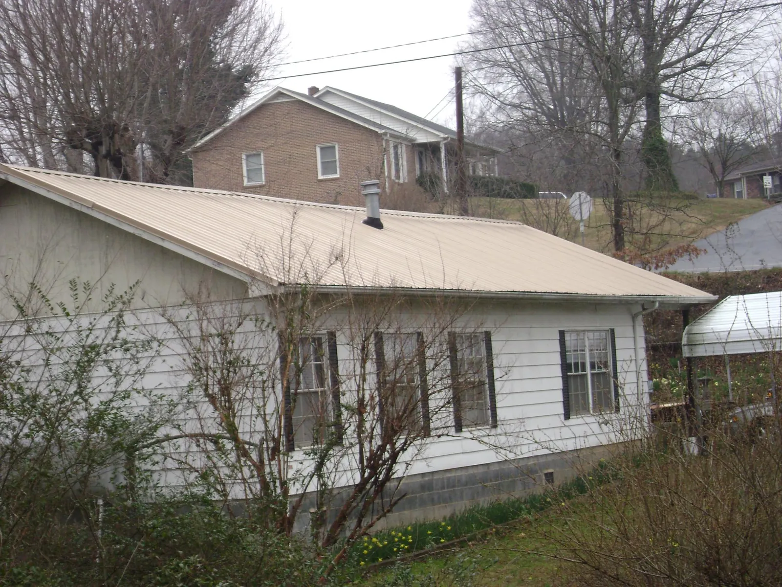 Tan metal roof on a white sided house set into a hillside — Commercial Roofing by Roofing Brothers in Lookout Mountain